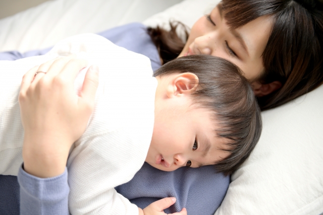 子育て 幼児を母親が抱いて横になっている